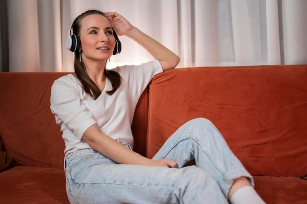 Una joven bonita escuchando música con auriculares y relajándose mientras está sentada en el sofá en casa