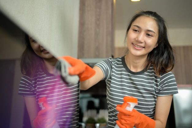 Una joven bonita con guantes de goma limpiando el horno con un trapo en la cocina