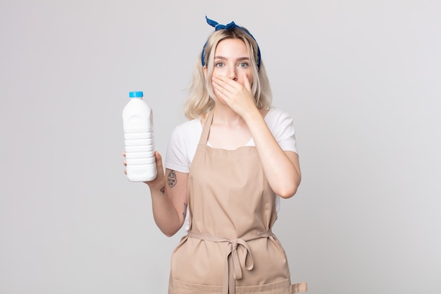 Joven bonita a mujer albina cubriendo la boca con las manos con un sorprendido con una botella de leche