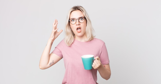 Joven bonita a mujer albina gritando con las manos en el aire con una taza de café