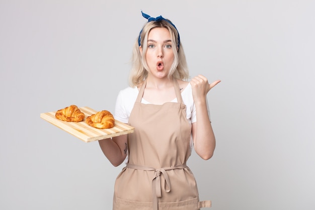 Joven bonita a mujer albina mirando asombrado con incredulidad con una bandeja de croissants