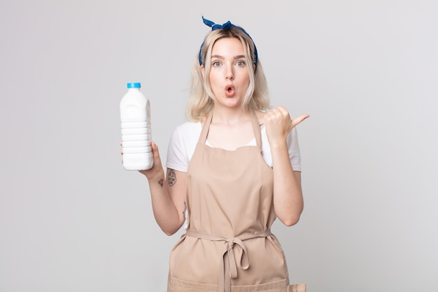 Joven bonita a mujer albina mirando asombrado con incredulidad con una botella de leche