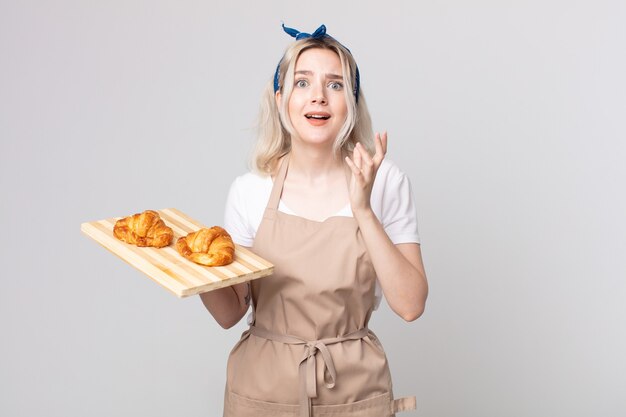 Joven bonita a mujer albina que parece desesperada, frustrada y estresada con una bandeja de croissants