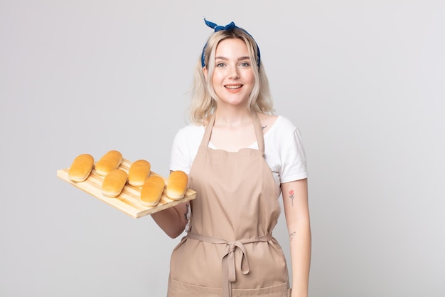 Joven bonita a mujer albina que parece feliz y gratamente sorprendida con una bandeja de bollos de pan