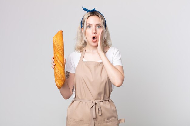 Joven bonita a mujer albina que se siente conmocionada y asustada con una baguette de pan