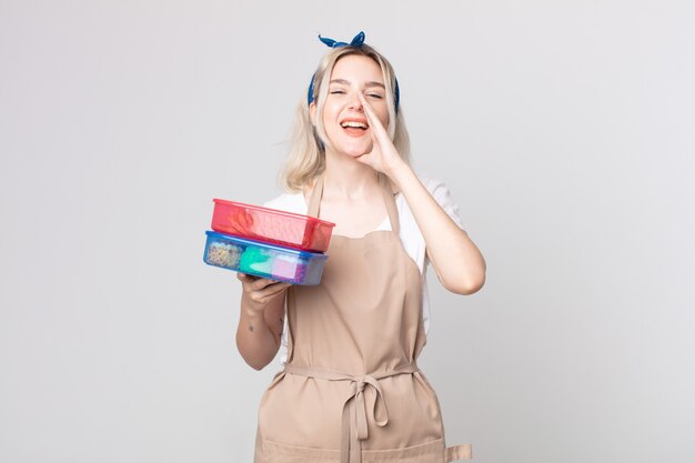 Joven bonita a mujer albina que se siente feliz, dando un gran grito con las manos al lado de la boca sosteniendo comida tupperwares