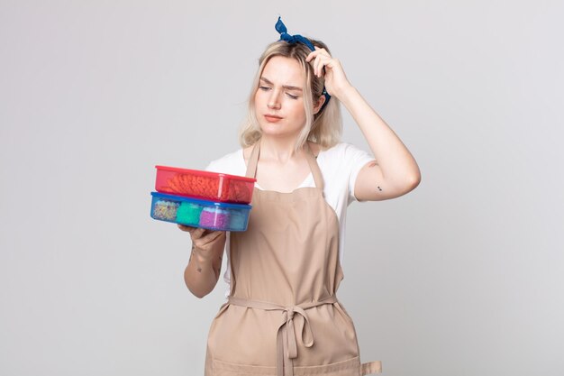 Joven bonita a mujer albina que se siente perpleja y confundida, rascándose la cabeza sosteniendo tupperwares de comida