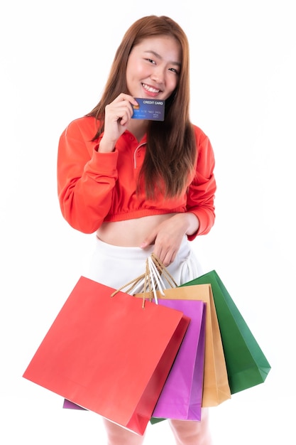 Joven bonita a mujer asiática sosteniendo muchas bolsas de compras y mostrando tarjeta de crédito para compras de pago sobre fondo blanco.