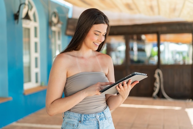 Una joven y bonita mujer brasileña al aire libre tocando la pantalla de la tableta con una expresión feliz