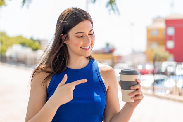 Joven y bonita mujer brasileña sosteniendo un café para llevar al aire libre y apuntándolo