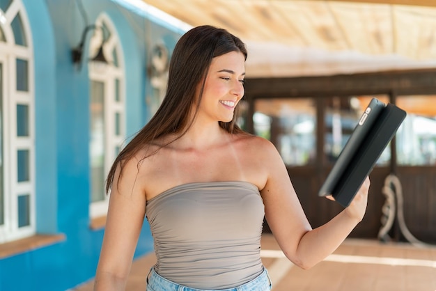 Joven y bonita mujer brasileña sosteniendo una tableta al aire libre con expresión feliz