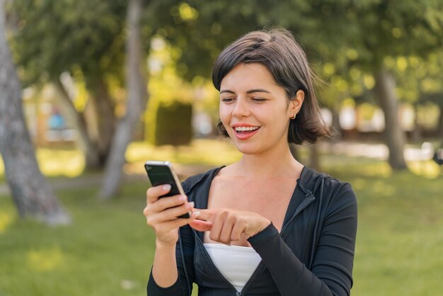 Joven y bonita mujer búlgara al aire libre enviando un mensaje o correo electrónico con el móvil