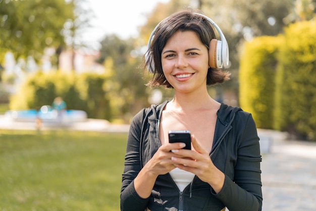 Joven y bonita mujer búlgara al aire libre escuchando música con un móvil y mirando al frente