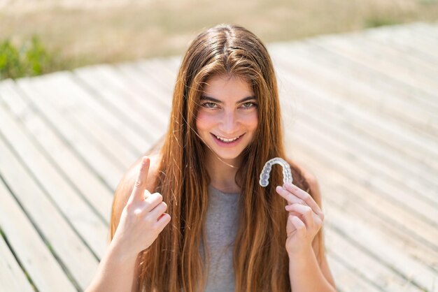 Joven y bonita mujer caucásica con aparatos dentales invisibles al aire libre señalando una gran idea