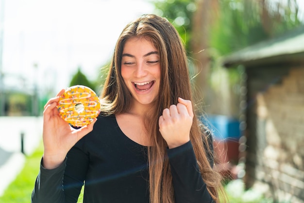 Joven y bonita mujer caucásica con una rosquilla al aire libre celebrando una victoria