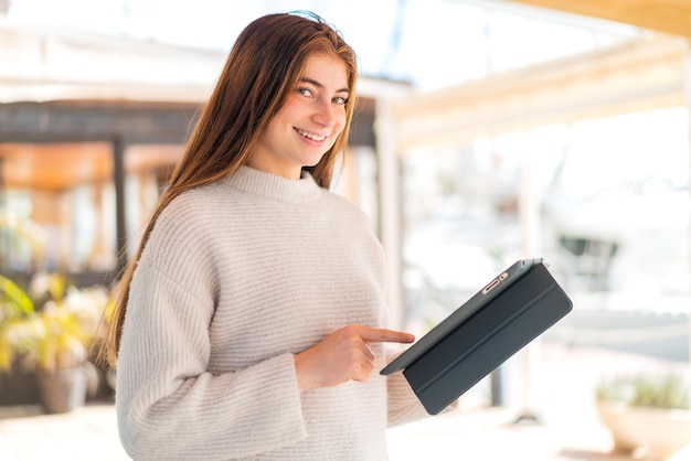 Joven y bonita mujer caucásica sosteniendo una tableta con expresión feliz