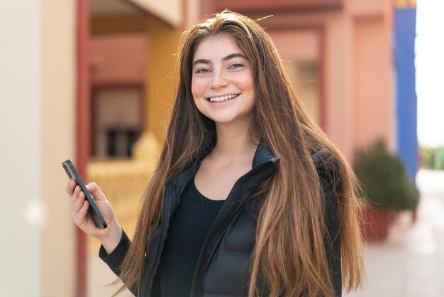 Joven y bonita mujer caucásica usando el teléfono móvil al aire libre sonriendo mucho