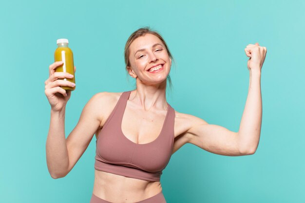 Joven bonita a mujer deportiva celebrando una victoria exitosa y sosteniendo batido