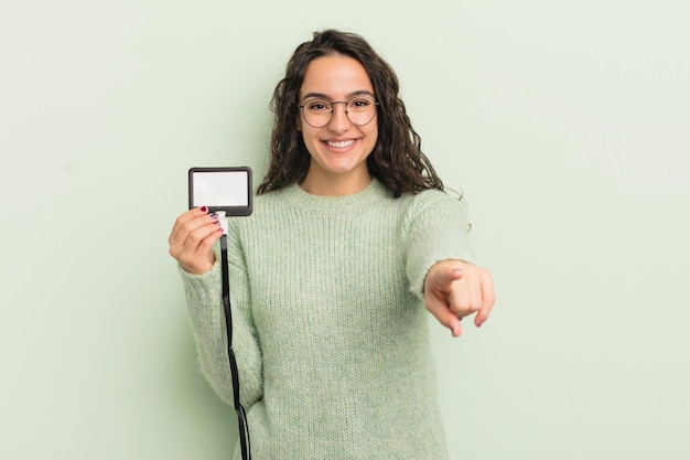 Joven bonita mujer hispana apuntando a la cámara eligiendo su identificación de tarjeta de acreditación