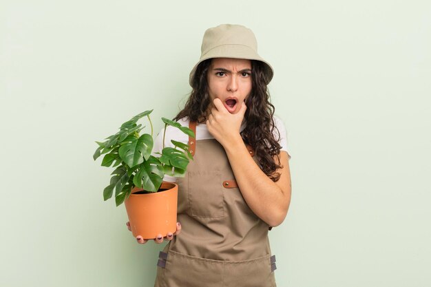 joven y bonita mujer hispana con la boca y los ojos bien abiertos y la mano en la barbilla. concepto de agricultor o jardinero