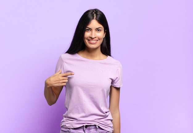 Joven bonita a mujer hispana que parece orgullosa, segura y feliz, sonriendo y apuntando a sí misma o haciendo la señal número uno