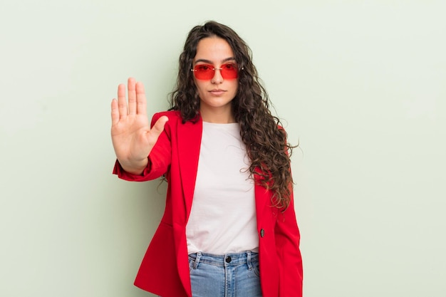 Joven bonita mujer hispana que parece seria mostrando la palma abierta haciendo un gesto de parada. genial mujer de negocios