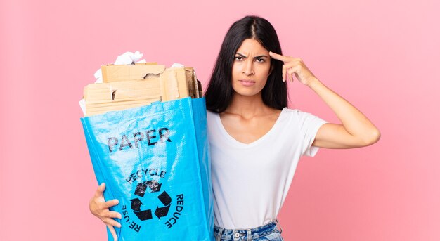 Foto joven bonita a mujer hispana que se siente confundida y perpleja, mostrando que está loco y sosteniendo una bolsa de papel para reciclar