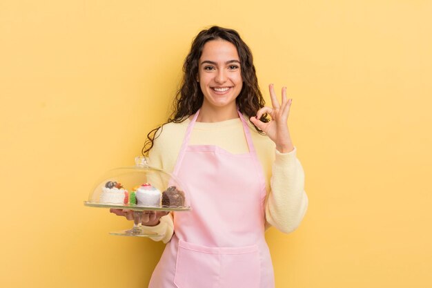 joven y bonita mujer hispana que se siente feliz, mostrando aprobación con un gesto bien. concepto de chef y pasteles