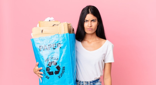 Joven bonita a mujer hispana que se siente triste, molesta o enojada y mirando hacia un lado y sosteniendo una bolsa de papel para reciclar