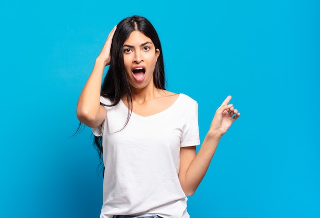 Joven bonita a mujer hispana riendo, luciendo feliz, positiva y sorprendida, dándose cuenta de una gran idea apuntando al espacio de copia lateral