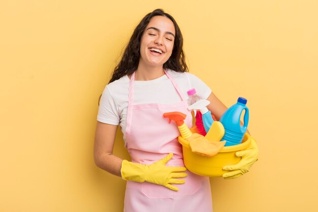 Joven y bonita mujer hispana riéndose a carcajadas de una broma hilarante que hace las tareas del hogar y un concepto de productos limpios