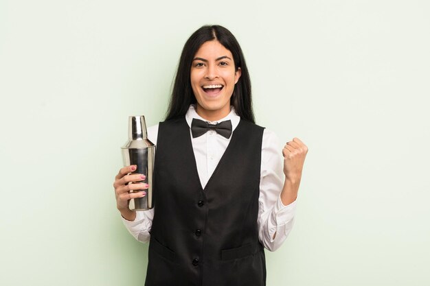 Joven bonita mujer hispana sintiéndose sorprendida, riendo y celebrando el concepto de barman de cócteles de éxito