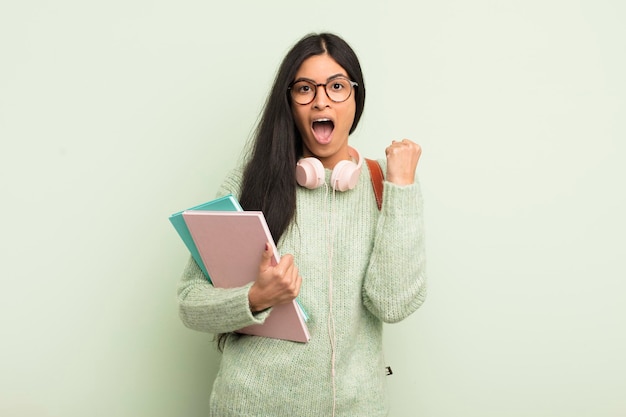 Joven bonita mujer hispana sintiéndose sorprendida, riendo y celebrando el concepto de estudiante de éxito