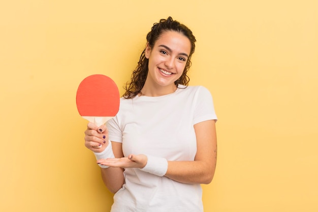 Joven bonita mujer hispana sonriendo alegremente sintiéndose feliz y mostrando un concepto de ping pong