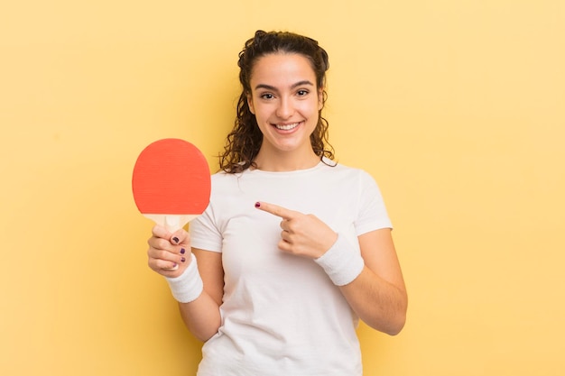 Joven bonita mujer hispana sonriendo alegremente sintiéndose feliz y señalando el concepto de ping pong lateral