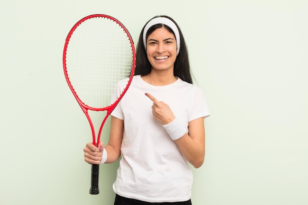 Joven bonita mujer hispana sonriendo alegremente sintiéndose feliz y señalando el concepto de tenis lateral