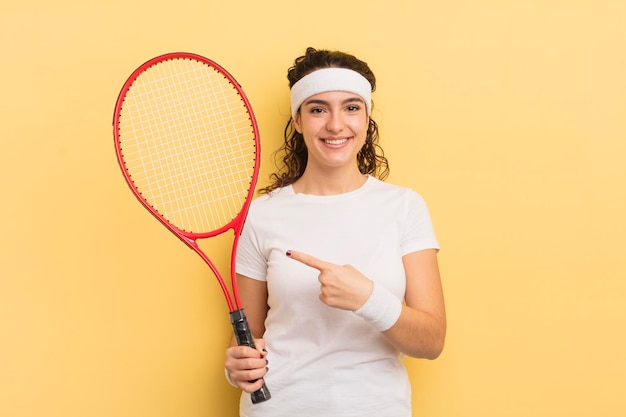 Joven bonita mujer hispana sonriendo alegremente sintiéndose feliz y señalando el concepto de tenis lateral