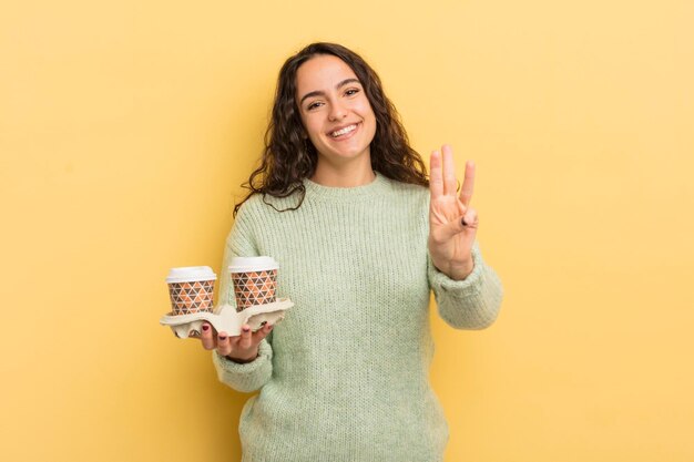 Joven bonita mujer hispana sonriendo y luciendo amigable mostrando el concepto de café para llevar número tres