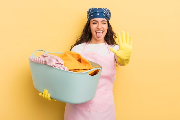 Joven bonita mujer hispana sonriendo y luciendo amigable mostrando el concepto de lavado y ropa número cinco