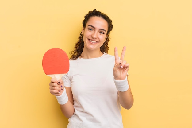 Joven bonita mujer hispana sonriendo y luciendo amigable mostrando el concepto de ping pong número dos