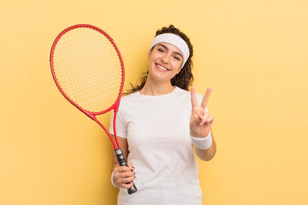 Joven bonita mujer hispana sonriendo y luciendo amigable mostrando el concepto de tenis número dos