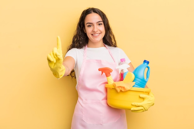 Joven bonita mujer hispana sonriendo y luciendo amigable mostrando el trabajo doméstico número uno y el concepto de productos limpios