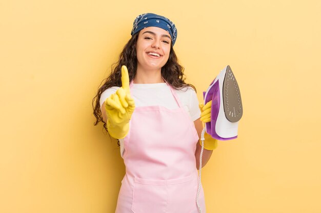 Joven bonita mujer hispana sonriendo con orgullo y confianza haciendo el concepto número uno de hierro y ropa