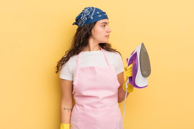 Joven bonita mujer hispana en la vista de perfil pensando imaginando o soñando despierto con el concepto de hierro y ropa