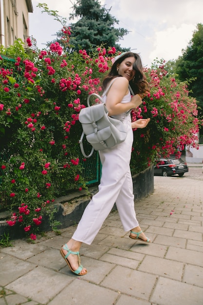 Joven bonita a mujer sonriente cerca de espacio de copia de arbusto de rosas rojas florecientes