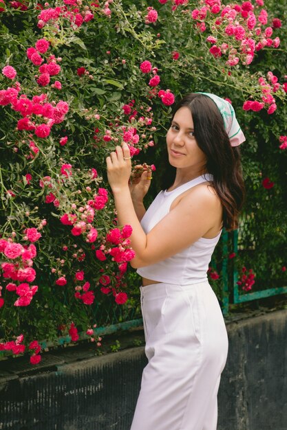 Joven bonita a mujer sonriente cerca de espacio de copia de arbusto de rosas rojas florecientes