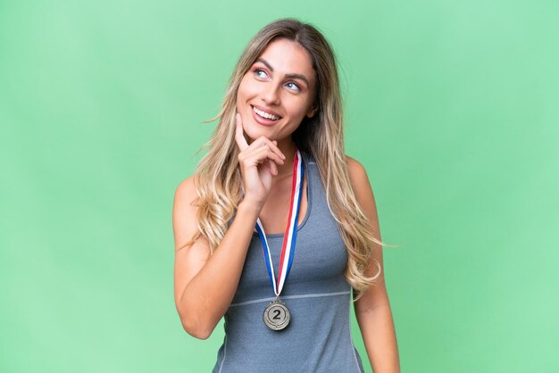 Joven bonita mujer uruguaya deportiva con medallas sobre un fondo aislado pensando en una idea mientras mira hacia arriba