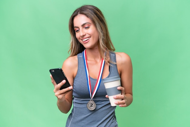 Joven bonita mujer uruguaya deportiva con medallas sobre un fondo aislado sosteniendo café para llevar y un móvil