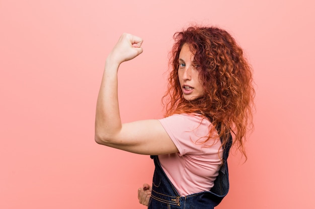 Joven bonita pelirroja jengibre mujer vestida con un mono de jeans levantando el puño después de una victoria