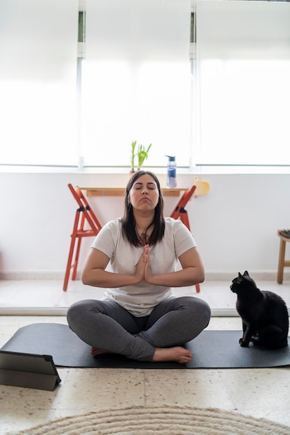 una joven bonita practicando ejercicio y yoga en su salón con un gato negro